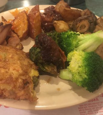 A plate of assorted foods including grilled meat, broccoli, roasted potatoes, fried rice cake, and orange-glazed sweet potatoes.