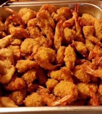 A tray filled with golden, crispy fried shrimp and fish, served with tongs for easy serving.