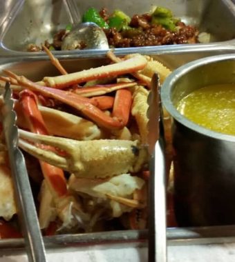 A serving tray filled with crab legs and claws, beside a bowl of yellow sauce, set in a buffet-style restaurant.