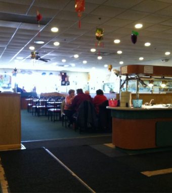 Interior of a restaurant featuring a buffet area, black chairs, patrons dining, and colorful decorations hanging from the ceiling.